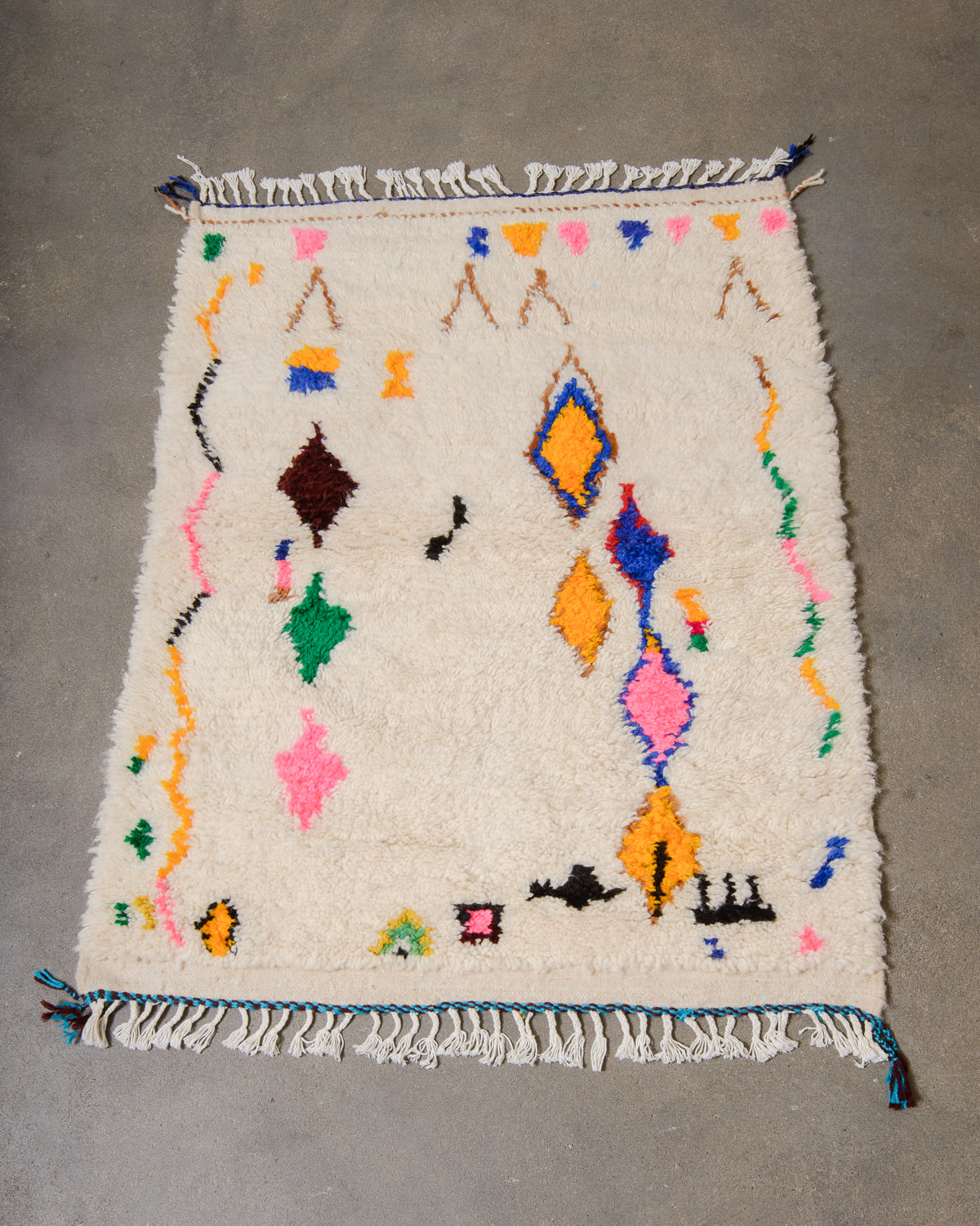 Cream wool Azilal rug with colourful cotton design laying on a concrete floor.